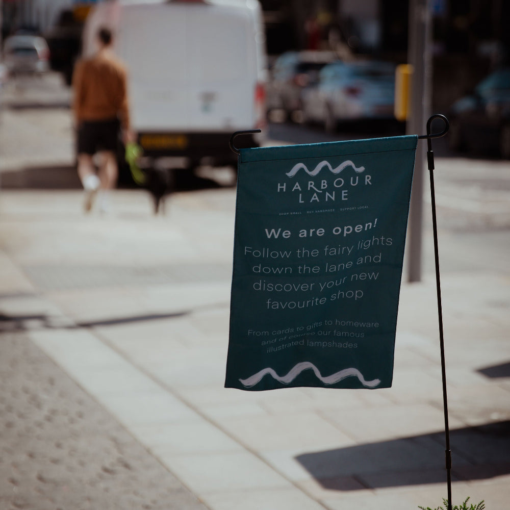 Harbour Lane promotional flag on a sidewalk with people and vehicles in the background