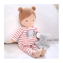 A super soft cotton doll. Eli wears a red and white striped babygro, has blonde boucle hair in buns and holds a little Elephant friend.