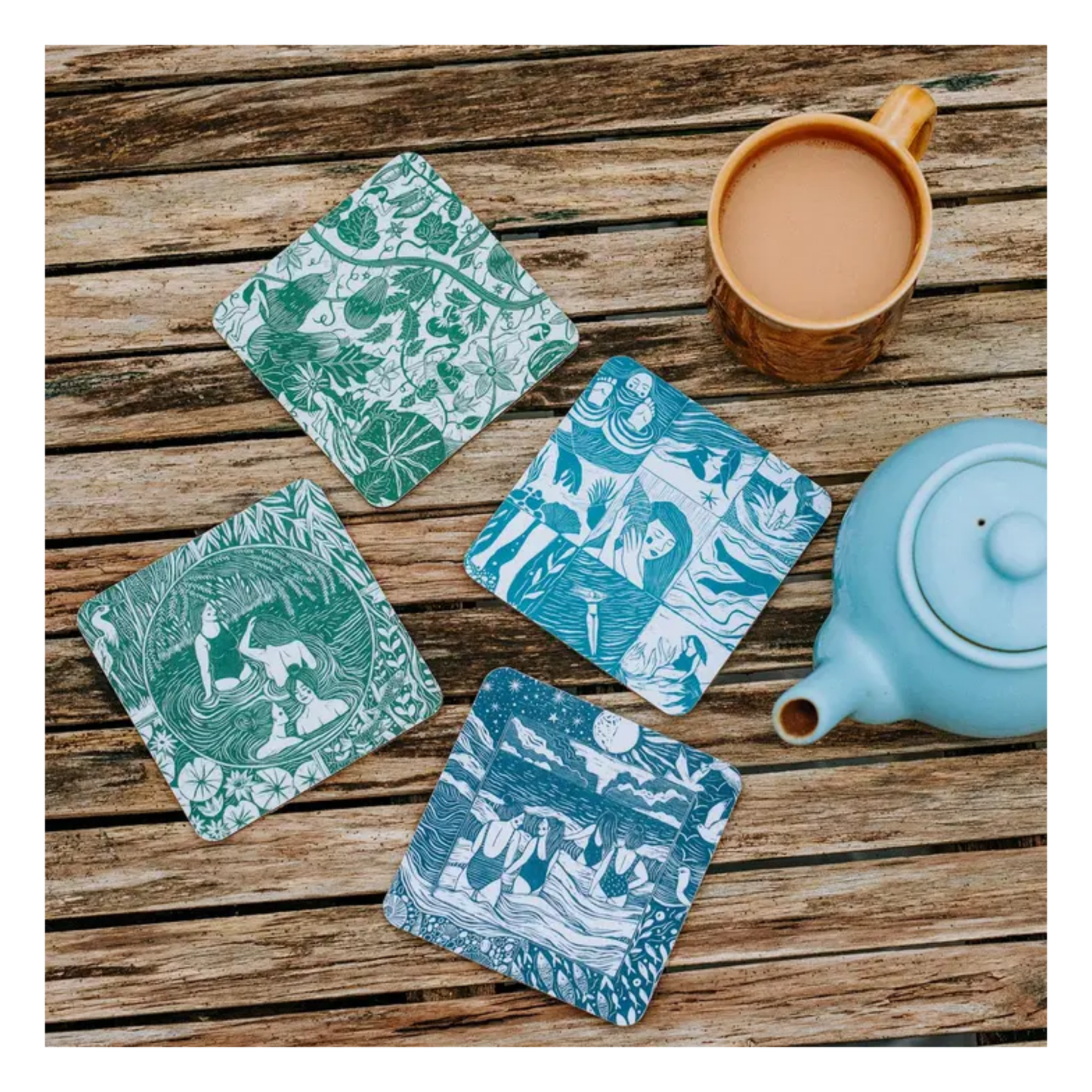 Four illustrated coasters on a wooden surface with a cup and teapot.