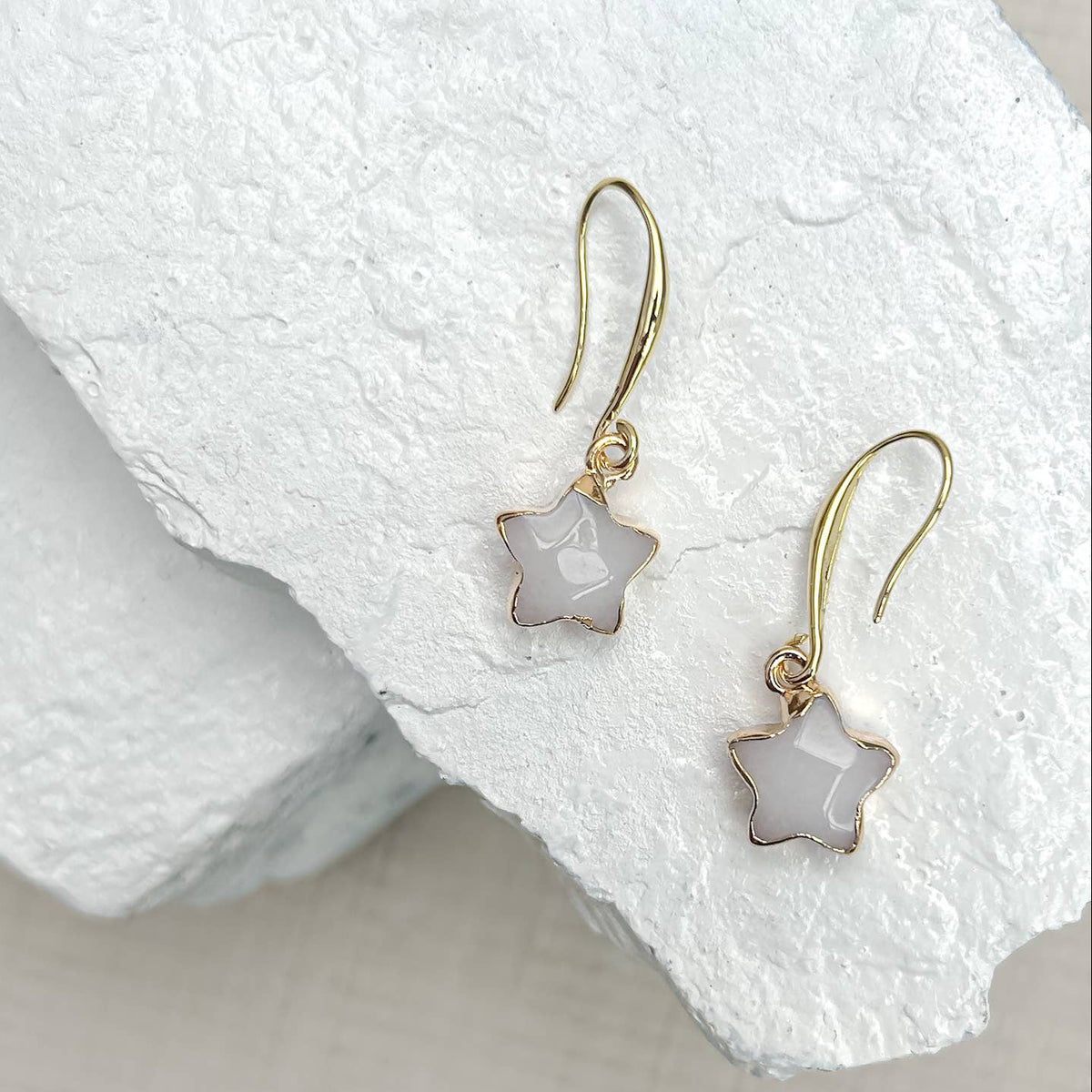 Gold earrings with star-shaped white stones on a textured white surface