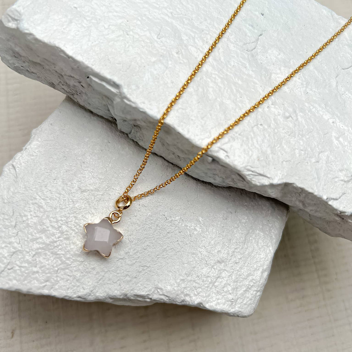 Gold necklace with a star-shaped pendant on a textured white surface
