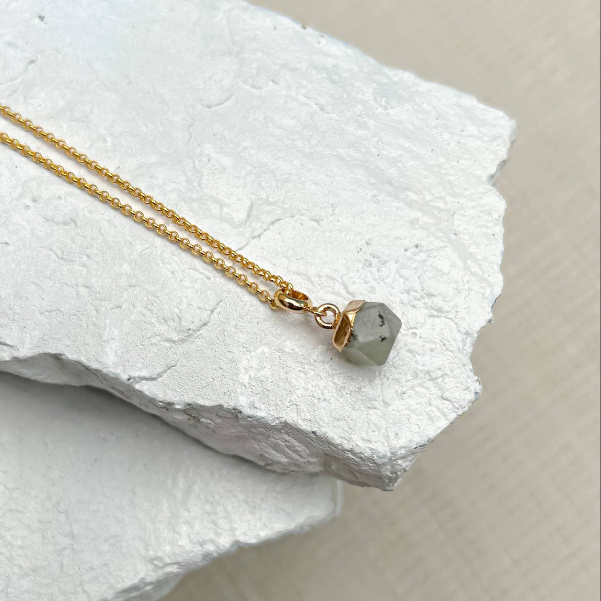 Gold necklace with a small stone pendant on a white stone surface