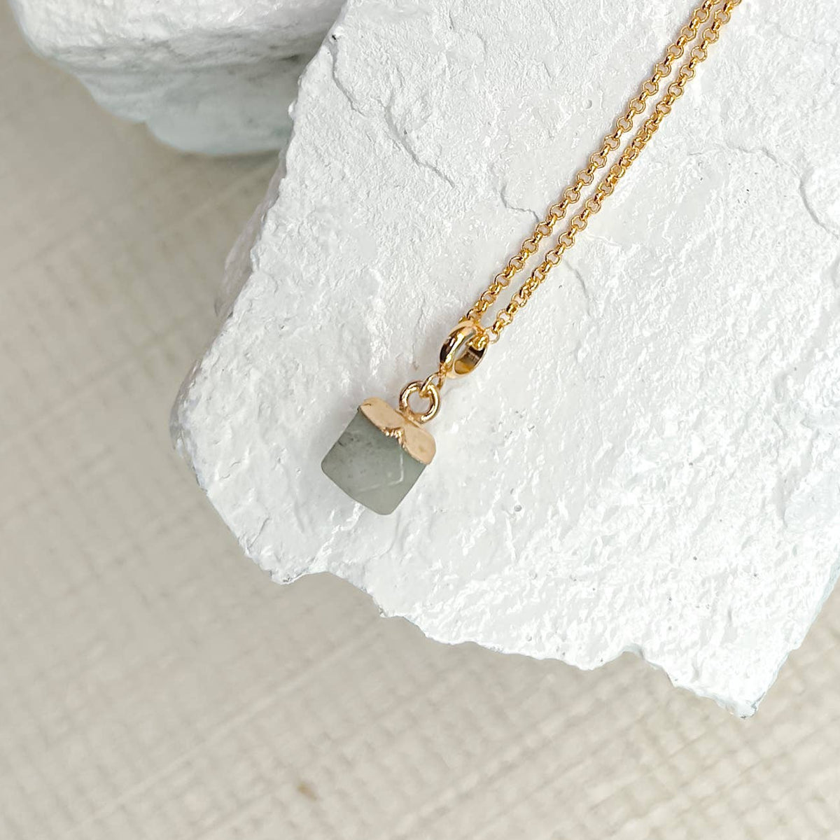 Gold necklace with a small pendant on a textured white surface