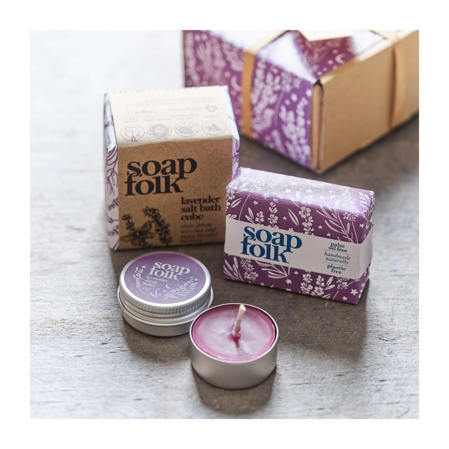 Soap Folk products including a bar of soap, salt bath cube, and candles on a wooden surface.
