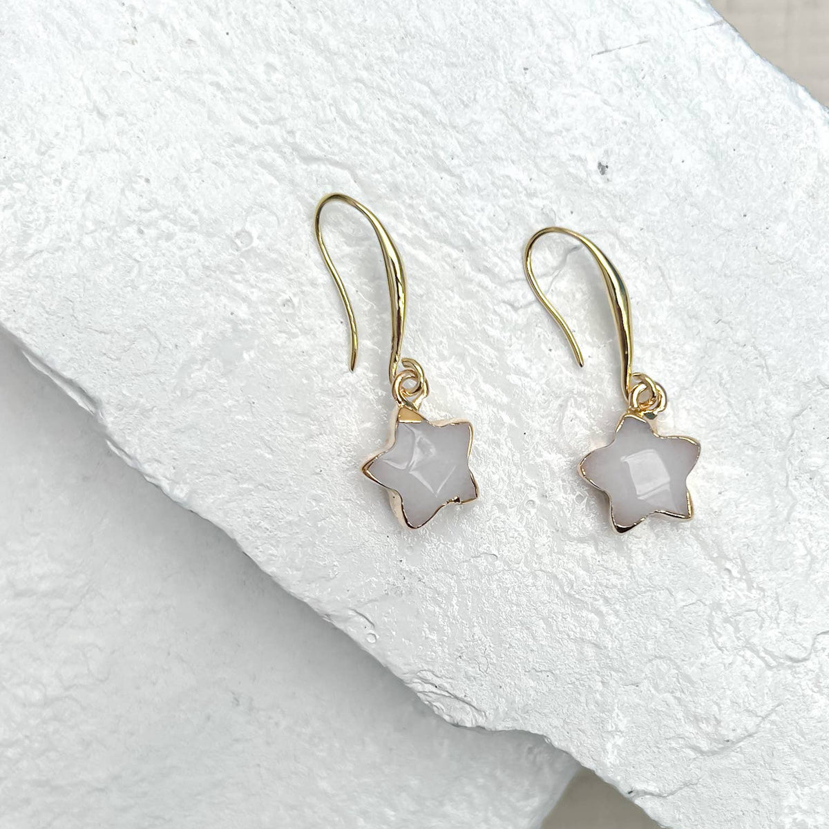 Star-shaped earrings with gold hooks on a white fabric background